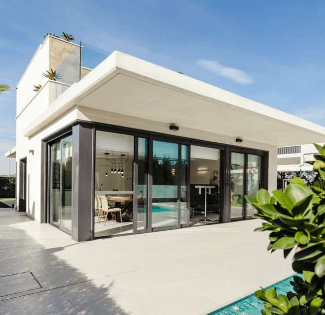 Modern minimalist house with large glass windows, terrace, and greenery.