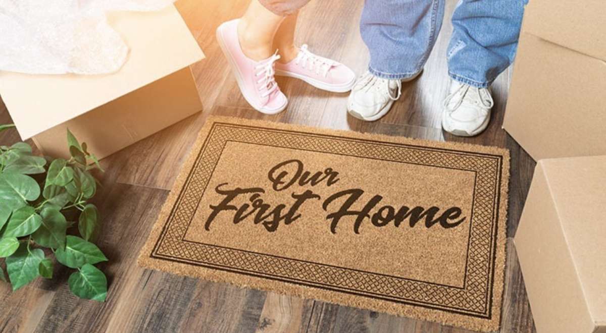 First home couple with doormat, houseplant, and moving boxes.
