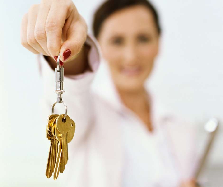 Hand holding gold keys, professional woman in blurred background. Real estate, property management.